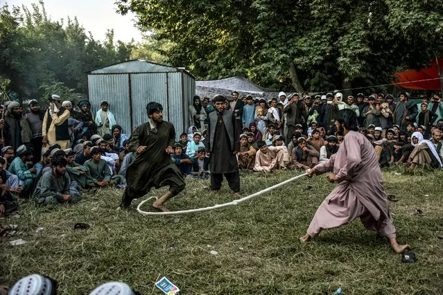 In this photo taken on June 2, 2020, men crowd to watch people playing a traditional rope game called Dora in a field, despite the spread of the COVID-19 coronavirus in the country, in Arghandab district in the Taliban stronghold of Kandahar province. The Taliban boasted of their readiness to fight the deadly coronavirus when it first reached Afghanistan, but now the insurgents are struggling to curb its spread in their strongholds. (Photo by Javed Tanveer/AFP Photo)