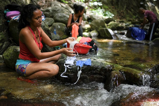 A woman washes her protective face masks with runoff water from the Avila mountain in Caracas, Venezuela, Sunday, June 21, 2020. Water shortages have continued to deepen in Venezuela at a time when the threat of the coronavirus makes washing hands even more critical. (Photo by Matias Delacroix/AP Photo)