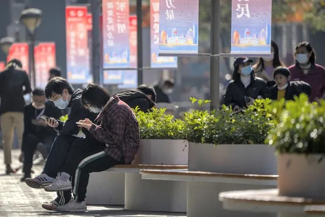 People wearing face masks sit on a bench at a pedestrian shopping street in Beijing, Saturday, November 5, 2022. (Photo by Mark Schiefelbein/AP Photo)