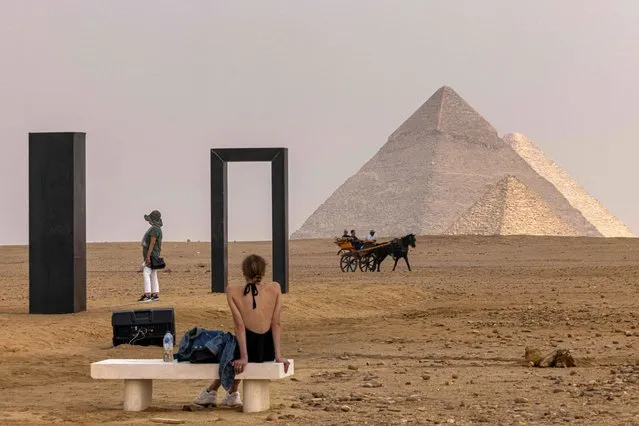 A woman looks on while a horse-drawn carriage passes by Italian artist Emilio Ferro's artwork installation “Portal of Light” at the Giza pyramids necropolis during the second edition of the Art D’Égypte exhibition “Forever is Now” on October 27, 2022. (Photo by Khaled Desouki/AFP Photo)