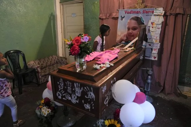 A girl looks into the open casket of Yadimar Sierra, 11, during her wake inside her home in the Petare neighborhood of Caracas, Venezuela, Sunday, November 20, 2022. A week earlier, Yadimar was fatally hit by a stray bullet while she was sleeping in her home, according to her family. (Photo by Ariana Cubillos/AP Photo)