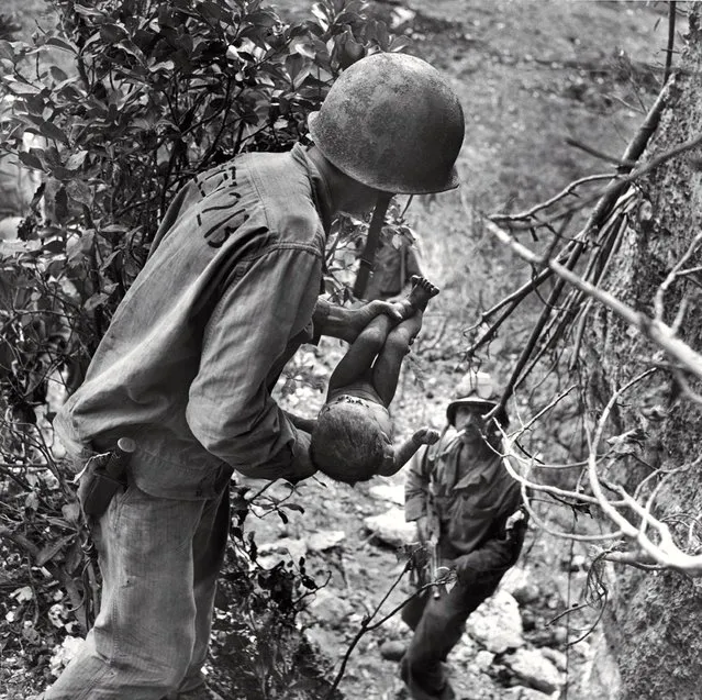 In a photo that somehow comprises both tenderness and horror, an American Marine cradles a near-dead infant pulled from under a rock while troops cleared Japanese fighters and civilians from caves on Saipan in the summer of 1944. The child was the only person found alive among hundreds of corpses in one cave. (Photo by W. Eugene Smith/Time & Life Pictures)