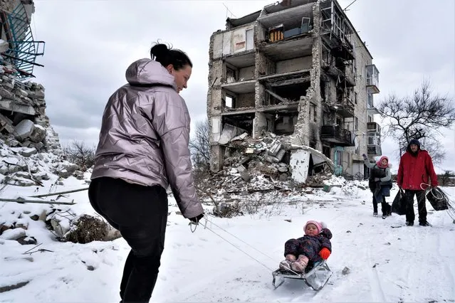 A family is seen outside of a destroyed apartment building, collecting scrap metal from inside after snowfall amid the ongoing Russia-Ukraine war in Izium, Ukraine on February 12, 2023. (Photo by Wolfgang Schwan/Anadolu Agency via Getty Images)