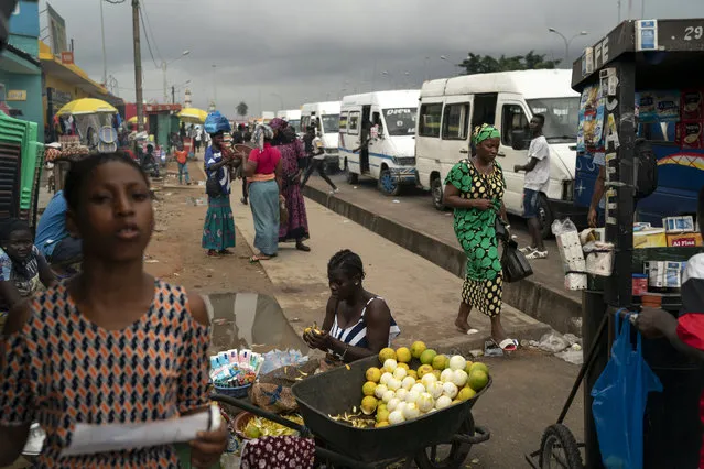 A woman peels oranges to sell on the sidewalk at Abobo neighborhood, a President Alassane Ouattara stronghold, in Abidjan, Ivory Coast, Monday, November 2, 2020. (Photo by Leo Correa/AP Photo)
