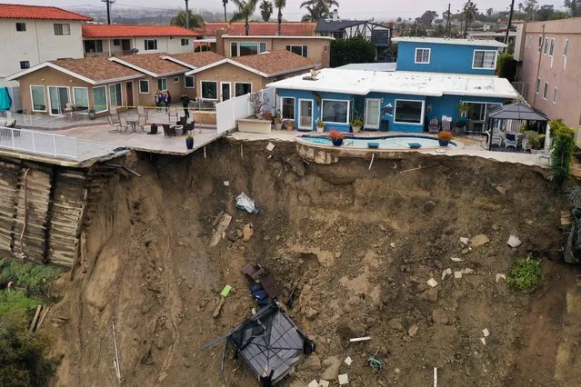 People (L) look at a swimming pool sitting on the edge of a landslide below an apartment building following heavy rains from a winter storm in Oceanside, California, on March 15, 2023. Residents were evacuated from homes overlooking the Pacific Ocean coastline on Buena Vista due to the landslide. The parade of winter storms that have pummeled California have caused hundreds of millions of dollars of damage as they washed out communities, brought down power lines and caused landslides. More than 20 people have died. (Photo by Patrick T. Fallon/AFP Photo)