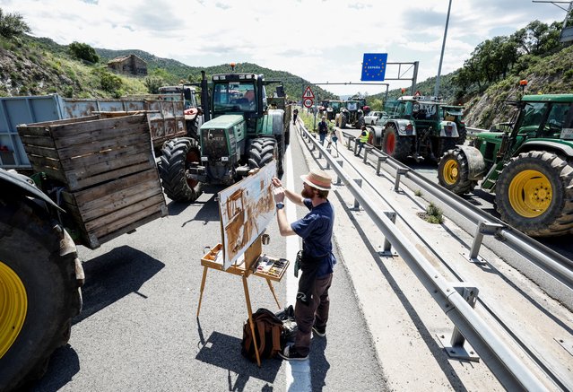 Dutch painter Cedric Visser paints as farmers with tractors block the highway AP-7, near the border between Spain and France, during a demonstration demanding better conditions ahead European elections, in Le Perthus, Spain, on June 3, 2024. (Photo by Albert Gea/Reuters)