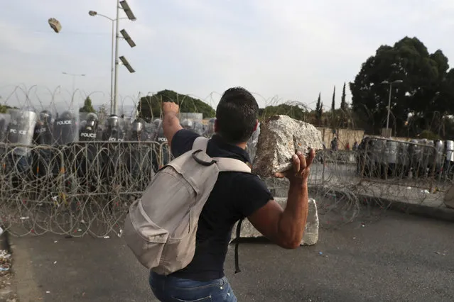 A protester throws a stone towards riot police during a protest against French President Macron's comments over Prophet Muhammad caricatures, near the Pine Palace, which is the residence of the French ambassador, in Beirut, Lebanon, Friday, October 30, 2020. A few hundred demonstrators held a protest called for by a Sunni Islamist party, Hizb ul-Tahrir, against French cartoons of the Prophet Muhammad. (Photo by Bilal Hussein/AP Photo)