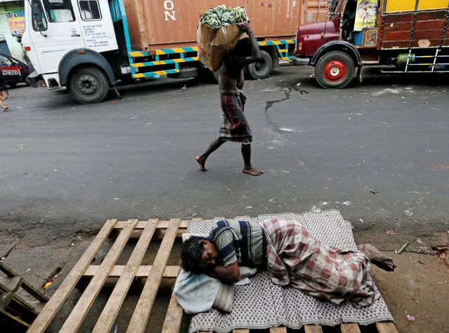 A man carries a sack of vegetables as another man sleeps on a road near a main market in Colombo, Sri Lanka August 31, 2016. (Photo by Dinuka Liyanawatte/Reuters)