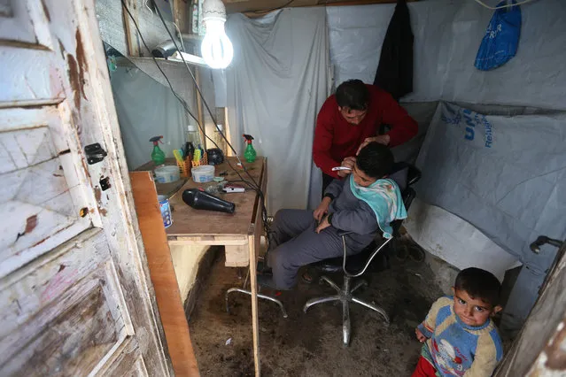 A Syrian barber cuts the hair a of boy, inside his small shop at a refugee camp in Deir Zannoun village, Bekaa valley, Lebanon, Tuesday, January 6, 2015. (Photo by Hussein Malla/AP Photo)
