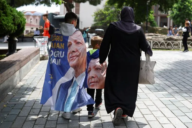 People walk while draped in banners featuring Turkish President Tayyip Erdogan, after he was declared the winner in the second round of the presidential election, in Istanbul, Turkey on May 29, 2023. (Photo by Hannah McKay/Reuters)