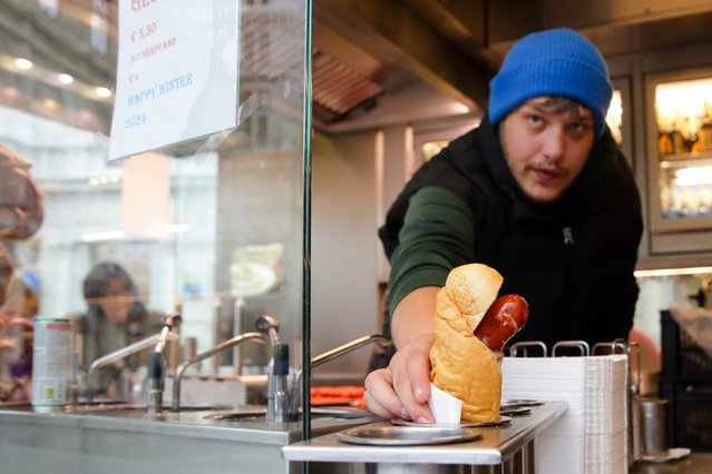 A vendor serves a hot dog at a traditional sausage stand (Wuerstelstand), which are named as intangible cultural heritage by the Austrian UNESCO Commission, in Vienna, Austria, Thursday, November 28, 2024. (Photo by Heinz-Peter Bader/AP Photo)