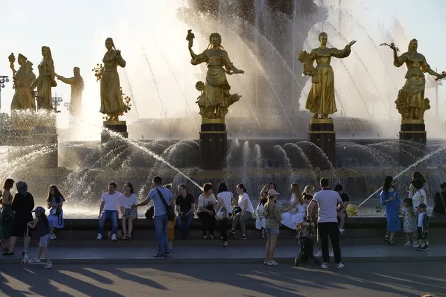 People cool themselves at a fountain “Friendship of Peoples” at VDNKh (The Exhibition of Achievements of National Economy) in Moscow, Russia, Sunday, June 20, 2021. The hot weather in Moscow is continuing, with temperatures forecast to reach over 30 degrees Celsius (86 Fahrenheit). (Photo by Alexander Zemlianichenko/AP Photo)