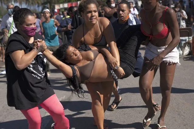 A woman who fainted during an eviction is carried away from the crowd for medical attention as they are evicted from land designated for a Petrobras refinery, where a settlement coined the “First of May Refugee Camp”, was created, the name referring to the date people moved here and set up tents and shacks to live in during the new coronavirus pandemic in Itaguai, Rio de Janeiro state, Brazil, Thursday, July 1, 2021. (Photo by Silvia Izquierdo/AP Photo)