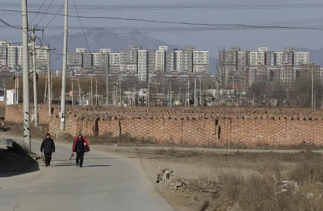 People walk past stacks of bricks in a field near new residential compounds, at a village in Beijing, China, January, 18, 2016. On the outskirts of Beijing, the disused factories of Chaomidian show the impact of China's drive to shut down thousands of small firms causing big pollution. Amid scrapheaps and idle machinery, the community has clean air these days – and no jobs. (Photo by Jason Lee/Reuters)