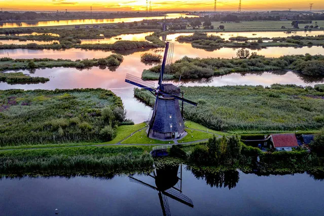 The sun rises behind a wind pump in Kinderdijk, Netherlands, Monday, August 14, 2023. About a third of the country is below sea level and wind pumps prevent regions from being flooded. (Photo by Michael Probst/AP Photo)