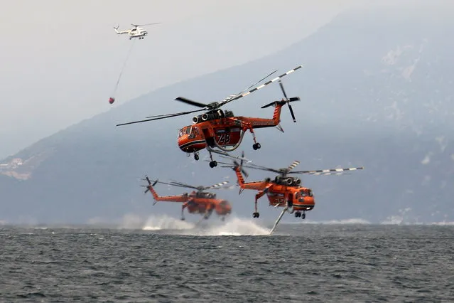 Firefightering helicopters are filled with water off the beach of the village of Pefki, on the island of Evia, Greece, August 10, 2021. (Photo by Nicolas Economou/Reuters)