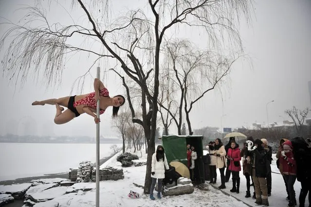 This picture taken on December 17, 2013 shows people watching a pole dancer (L) practise after it snowed in Tianjin during a promotional event by members of China's national pole dancing team and students of the sport. (Photo by AFP Photo)