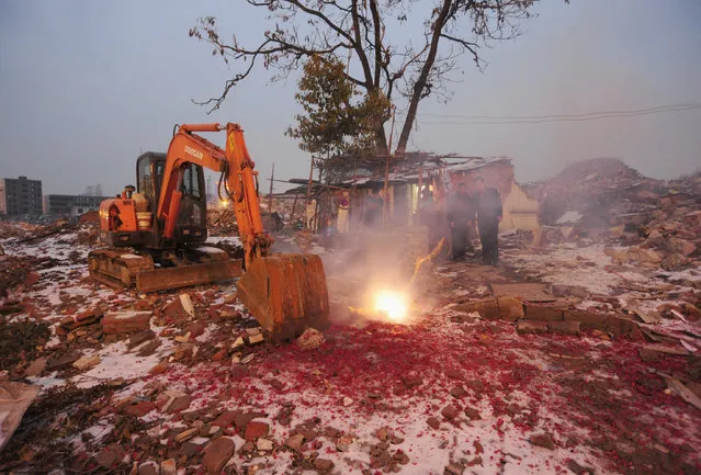 Cao Wenxia (L), the owner of a nail house, lights firecrackers to celebrate Chinese New Year near an excavator used for demolishing buildings near his house in Hefei, Anhui province, February 13, 2010. Cao's family refused to move due to unsatisfactory compensation for their house, the last house in the area. (Photo by Reuters/Stringer)