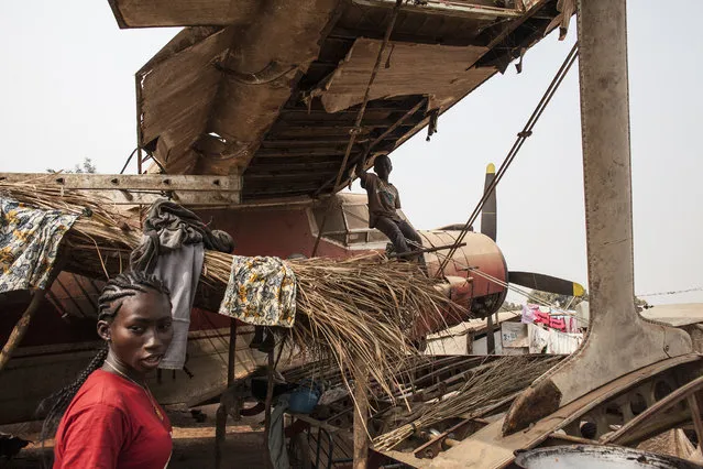 A woman walks under the wing of a plane wreckage being used as housing in M'Poko Internally Displaced Persons camp in Bangui, Central African Republic on Saturday, February 13, 2016. (Photo by Jane Hahn/The Washington Post)