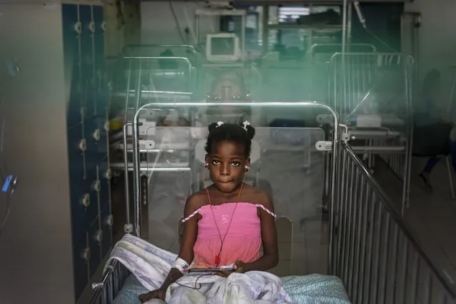 A girl rests on a bed as she listens to music at the Saint Damien Pediatric Hospital of Port-au-Prince, Haiti, Sunday, October 24, 2021. Haiti's capital has been brought to the brink of exhaustion by fuel shortages and the capital's main pediatrics hospital says it has only three days of fuel left to run ventilators and medical equipment. (Photo by Matias Delacroix/AP Photo)