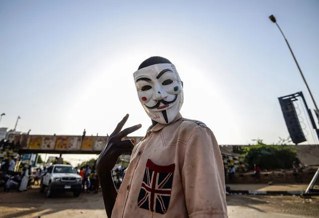 A Sudanese protester wears a Guy Fawkes mask outside the army headquarters in Khartoum on May 6, 2019. Defiant Sudanese protesters broke their fast on the first day of Ramadan today with chicken soup and beans, vowing to press on with their campaign for a civilian rule. As the call for the evening Maghreb prayer echoed, crowds of protesters gathered at the sit-in area in central Khartoum for iftar after a day of sweltering heat, an AFP correspondent reported. (Photo by Mohamed el-Shahed/AFP Photo)