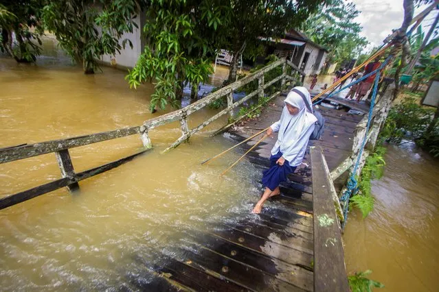 A student walks past on the broken bridge hit by a river overflow following floods in Jaranih village, Central Hulu Sungai, South Kalimantan province, Indonesia on November 17, 2021. (Photo by Bayu Pratama S./Antara Foto via Reuters)