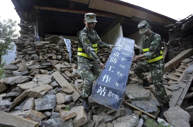 Border paramilitary policemen pick up a sign on the debris of their police station which was destroyed by a 7.9 magnitude earthquake that hit Nepal on April 25, in Gyirong county, Tibet Autonomous Region, China, May 14, 2015. (Photo by Reuters/Stringer)