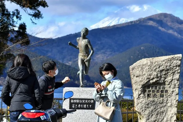 People gather by the memorial statue celebrating the Tokyo-Hakone collegiate Ekiden long-distance road relay run at the finish area before the arrival of runners in Hakone, Kanagawa prefecture on January 2, 2022. (Photo by Kazuhiro Nogi/AFP Photo)