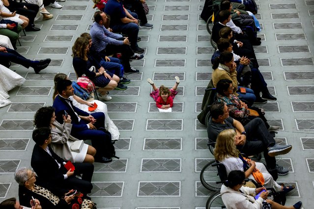 A child lies on the floor as people attend a weekly general audience in the Paul VI hall at the Vatican on May 1, 2024. (Photo by Remo Casilli/Reuters)