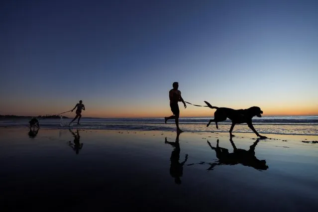 Clyde and his daughter Casey run with their dogs Prince and Jade after taking them for a swim at Cardiff State Beach in Encinitas, California, U.S., January 4, 2022. (Photo by Mike Blake/Reuters)