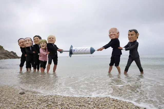 Activists wearing giant heads of the G7 leaders tussle over a giant COVID-19 vaccine syringe during an action of NGO's on Swanpool Beach in Falmouth, Cornwall, England, Friday, June 11, 2021. Leaders of the G7 begin their first of three days of meetings on Friday in Carbis Bay, in which they will discuss COVID-19, climate, foreign policy and the economy. Depicted from left to right, Japan's Prime Minister Yoshihide Suga, Italy's Prime Minister Mario Draghi, Canadian Prime Minister Justin Trudeau, German Chancellor Angela Merkel, British Prime Minister Boris Johnson, U.S. President Joe Biden and French President Emmanuel Macron. (Photo by Kirsty Wigglesworth/AP Photo)