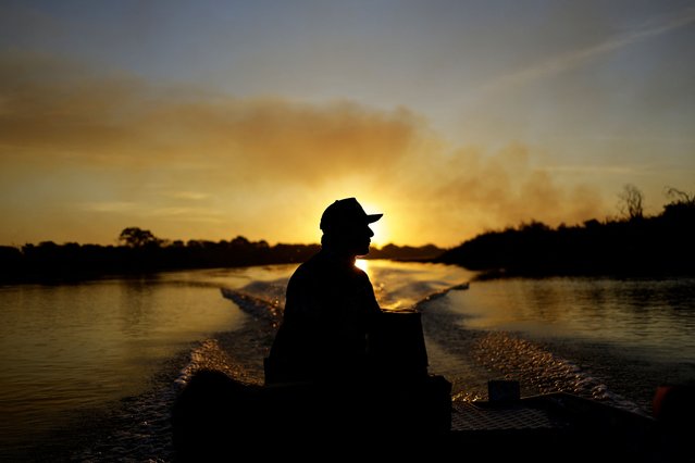 Fisher guide Amilton Brandao sails through the Paraguay River as smoke rises into the air from the fire in the Pantanal, the world's largest wetland, in Corumba, Mato Grosso do Sul state, Brazil, on June 11, 2024. (Photo by Ueslei Marcelino/Reuters)