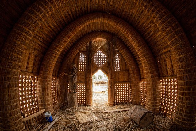 An Iraqi craftsman works on the construction of a traditional guest house (Mudhif), in front of the museum of the southern city of Basra, on December 29, 2021. The traditional Mudhif, a large ceremonial house for use by guests or as a gathering place for special occasions, is constructed from reeds, straw and other natural materials harvested from the marshes in southern Iraq. (Photo by Hussein Faleh/AFP Photo)