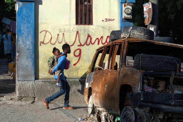 Seventeen-year-old Sevenson carries his 3-year-old little sister to school past the burned out remains of a car in a street of the Canape Vert neighborhood of Port-au-Prince, Haiti, on June 18, 2024. (Photo by Roberto Schmidt/AFP Photo)