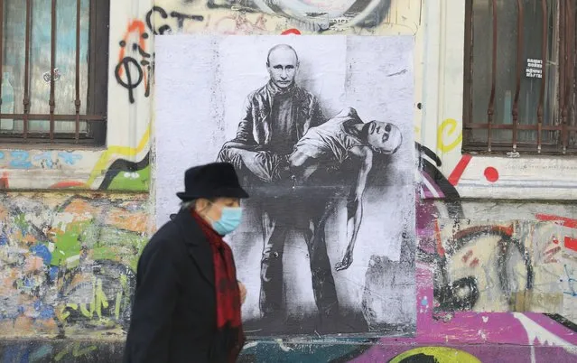 A woman walks past a poster depicting Russian President Vladimir Putin holding his own body, as Russia's invasion of Ukraine continues, in Sofia, Bulgaria, March 28, 2022. (Photo by Spasiyana Sergieva/Reuters)