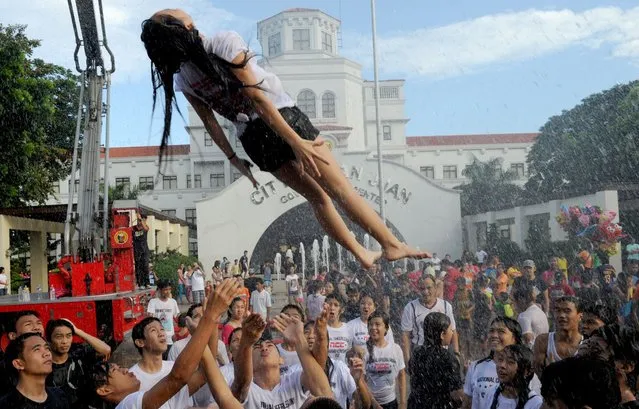 A woman hoisted into the air by friends after they were sprayed with water as residents celebrate the feast day of St. John the Baptist in Manila on June 24, 2014. Residents traditionally greet everyone with splashing water in a belief that it is a way of spreading good blessings on St. John's Day. (Photo by Jay Directo/AFP Photo)