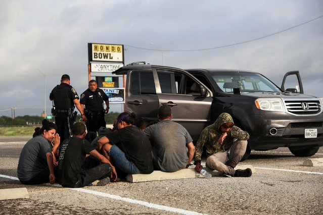 Asylum seeking migrants from Central America sit next to a vehicle that was stopped by police after crossing the Rio Grande into Eagle Pass, Texas, from Mexico along U.S. Route 90, in Hondo, Texas, U.S., June 1, 2022. U.S. authorities, blocked by a federal judge from lifting COVID-19 restrictions that empower agents at the U.S.-Mexico border to turn back migrants, continue to enforce the Title 42 rules which result in the fast expulsion of migrants to Mexico or other countries. (Photo by Shannon Stapleton/Reuters)