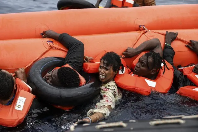 Migrants who were aboard a precarious rubber boat grab a centifloat as they are rescued by a team from the Sea Watch-3, around 35 miles away from Libya, in Libyan SAR zone, Monday, October 18, 2021. (Photo by Valeria Mongelli/AP Photo)