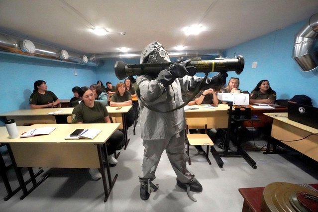 A Ukrainian serviceman in protective suit demonstrates grenade launcher to women during a training course for national resistance for local population in Kharkiv region, Ukraine, Friday, September 13, 2024.  (Photo by Andrii Marienko/AP Photo)