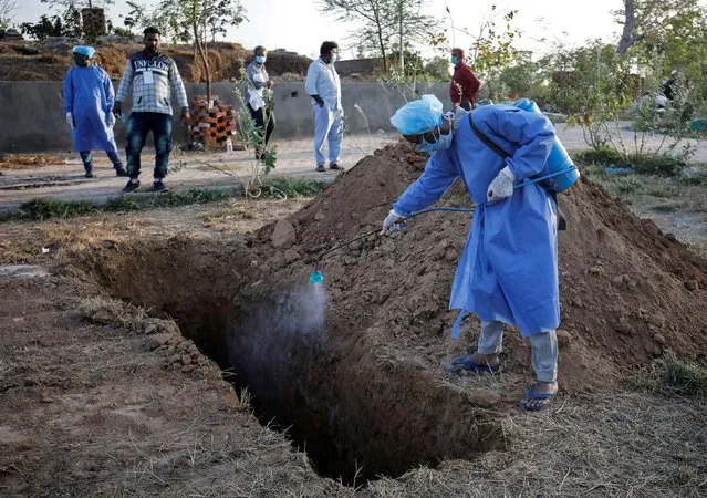 A municipal worker wearing a protective suit sprays disinfectant solution in a grave before the burial of a woman who died due to coronavirus disease (COVID-19), in Ahmedabad, India, March 28, 2020. (Photo by Amit Dave/Reuters)