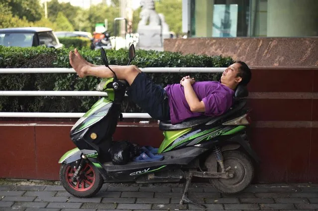 A man sleeps on an electric scooter on a sidewalk in Beijing on August 30, 2017. (Photo by Greg Baker/AFP Photo)