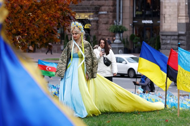 Young Ukrainian woman Olga (C) wears a dress in the country's national flag colors and a camouflage jacket of her fallen brother as she walks with her friend Anastasia (behind) on the Independence Square in Kyiv, Ukraine, 15 November 2023 amid the Russian invasion. They arrived from the city of Sumy to commemorate Olga's late brother Sergiy Myroshychenko who served with the 79th Air Assault Brigade and died near Maryinka in August 2023. They planned to place a flag with his name on it among thousands of similar flags placed on the square in commemoration of Ukrainian soldiers killed in action. Olga who made her dress for this special occasion and her friend also handed in a petition requesting her brother to be honored with a “Hero of Ukraine” award. Russian troops entered Ukraine in February 2022 starting a conflict that has provoked destruction and a humanitarian crisis. (Photo by Sergey Dolzhenko/EPA/EFE)