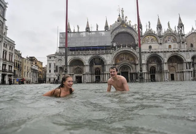 A young man and a woman enjoy swimming in flooded St. Mark's Square in Venice, Italy, Sunday, Nov. 11, 2012. High tides have flooded Venice, leading Venetians and tourists to don high boots and use wooden walkways to cross St. Mark's Square and other areas under water. Flooding is common this time of year and Sunday's level that reached a peak of 58.66 inches (149 centimeters) was below the 63 inches (160 centimeters) recorded four years ago in the worst flooding in decades. (Photo by Luigi Costantini/AP Photo)