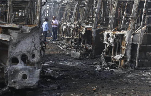 A television journalist reports amidst the charred remains of passenger buses owned by a transport company from the neighboring Tamil Nadu state, after they were set on fire by a mob in Bangalore, capital of the southern Indian state of Karnataka, India, Tuesday, September 13, 2016. Incidents of looting and vandalism eased Tuesday in parts of India's information technology hub of Bangalore after authorities imposed a curfew amid widespread protests overnight over India's top court ordering the southern state of Karnataka to release water from a disputed river to the neighboring state. (Photo by Aijaz Rahi/AP Photo)