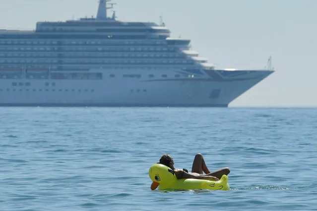 The Arcadia cruise ship anchored off the coast is seen behind a person relaxing in the sea, as it is unable to operate due to the coronavirus disease (COVID-19) outbreak, in Bournemouth, Britain, August 7, 2020. (Photo by Toby Melville/Reuters)