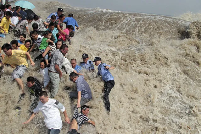 Police and residents run as waves from a tidal bore surge past a barrier as Typhoon Nanmadol approached the banks of Qiantang River in China's Zhejiang province, August 2011. (Photo by Reuters/China Daily)