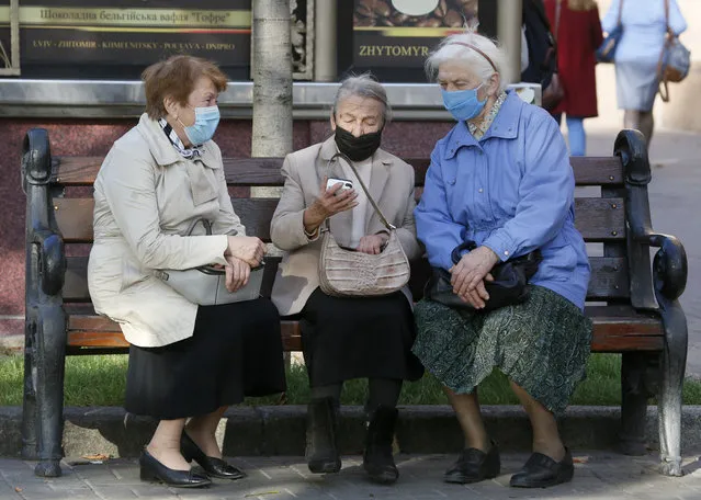 Elderly women wearing face masks to protect against coronavirus look at a phone sitting on a bench in capital Kyiv's main Khreshchatyk Street, Ukraine, Thursday, October 15, 2020. Ukraine has been registering a record number of COVID-19 cases every day. (Photo by Efrem Lukatsky/AP Photo)
