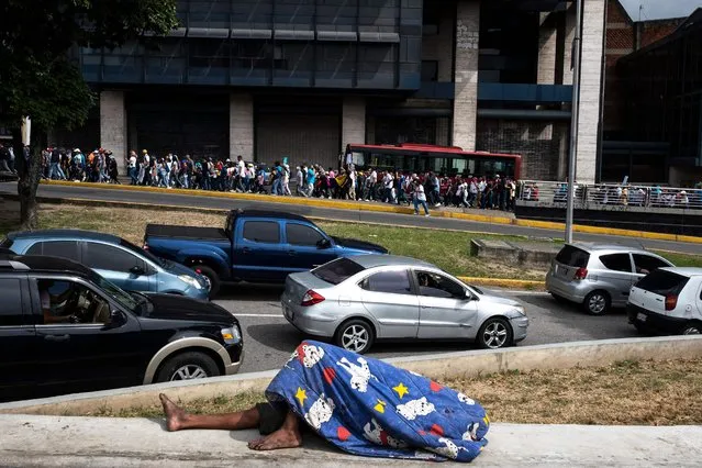 A man sleeps on a park bench while opposers of the government of Venezuelan President Nicolas Maduro hold a demonstration demanding a leveling of salaries in line with the raising inflation and the high cost of the basic family basket in Caracas on January 23, 2023. (Photo by Yuri Cortez/AFP Photo)