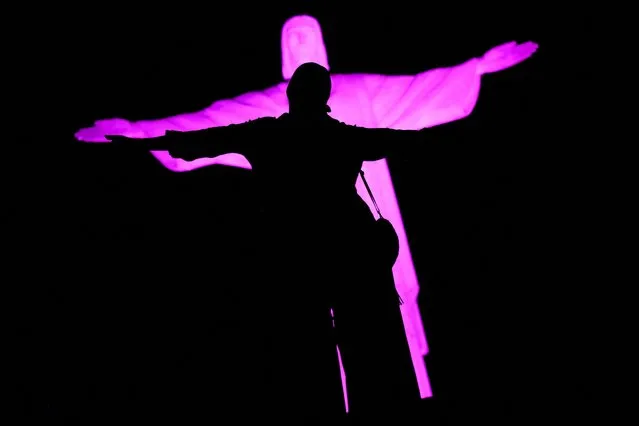 A person poses in front of the Christ the Redeemer statue lit in lilac to commemorate International Women's Day, in Rio de Janeiro, Brazil on March 8, 2023. (Photo by Lucas Landau/Reuters)