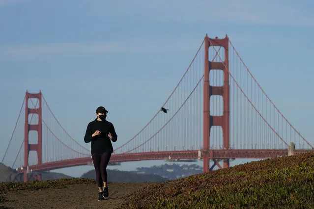 A person wearing a mask runs on a path in front of the Golden Gate Bridge during the coronavirus pandemic in San Francisco, Monday, November 30, 2020. (Photo by Jeff Chiu/AP Photo)